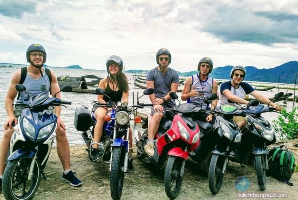 Groupe de touristes étrangers posant fièrement sur leurs scooters au bord de l'eau.